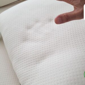 A hand lightly presses on a white organic latex pillow, showing its resilience and softness. Eco-friendly and made with natural materials.