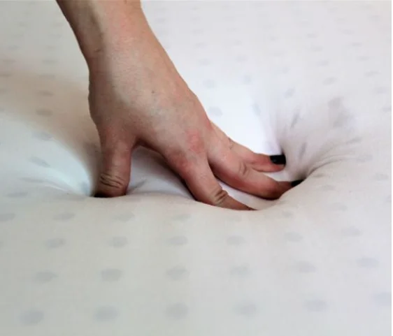 Une main pressant un surmatelas en latex doux et moelleux, montrant sa texture confortable.