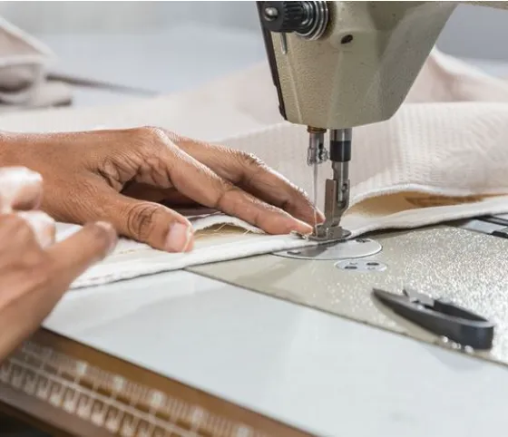 Un gros plan d'une aiguille de machine à coudre cousant à travers un tissu blanc.