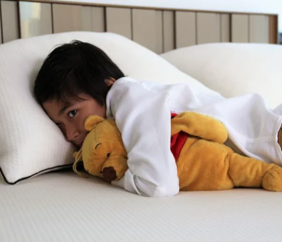 Une douce image d’un garçon profitant d’un sommeil réparateur sur un matelas en latex moelleux, câlinant son ours en peluche.