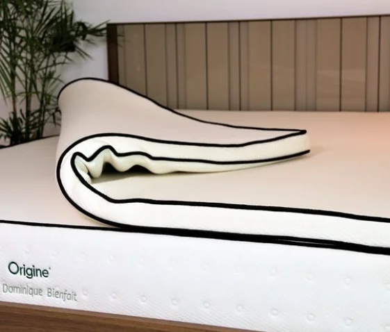 Gros plan d'un surmatelas en latex naturel avec un bord noir, enroulé.