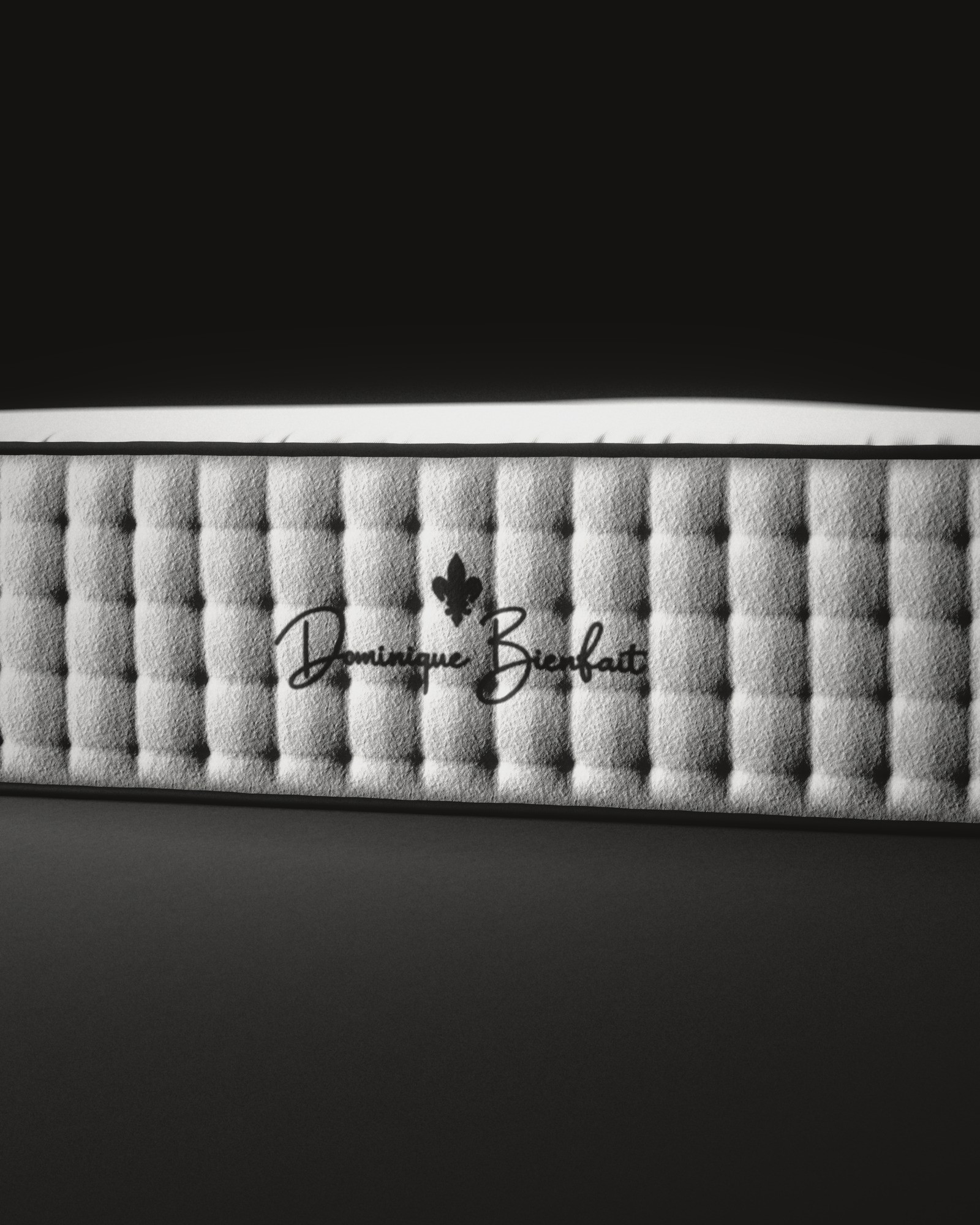 The foot end of a white mattress, close: a black fleur-de-lis and the name Dominique Bienfait on deep tufted cotton.