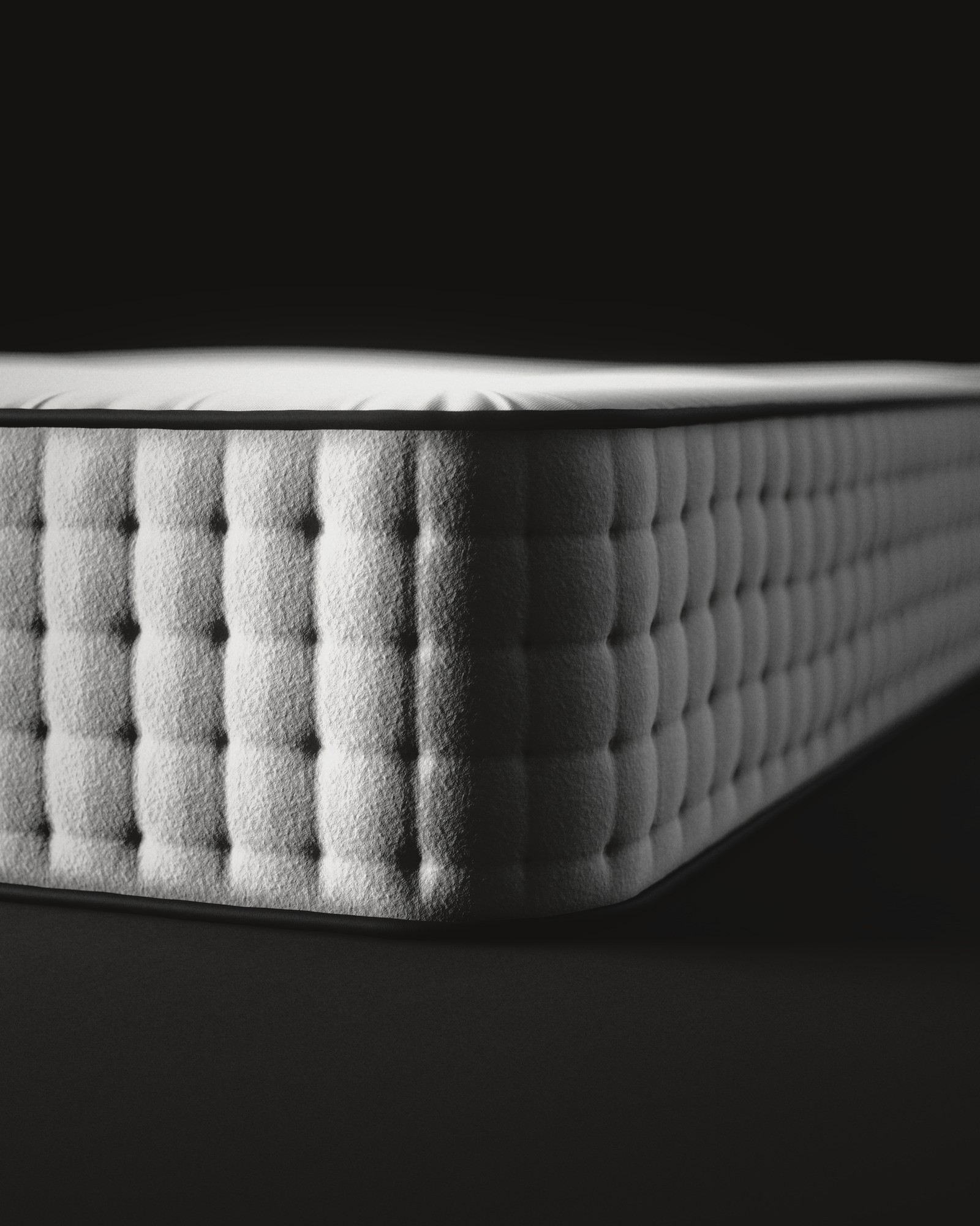 The corner of a white mattress cover, close: black piping round the top and rows of soft tufted cushions running away into the dark.