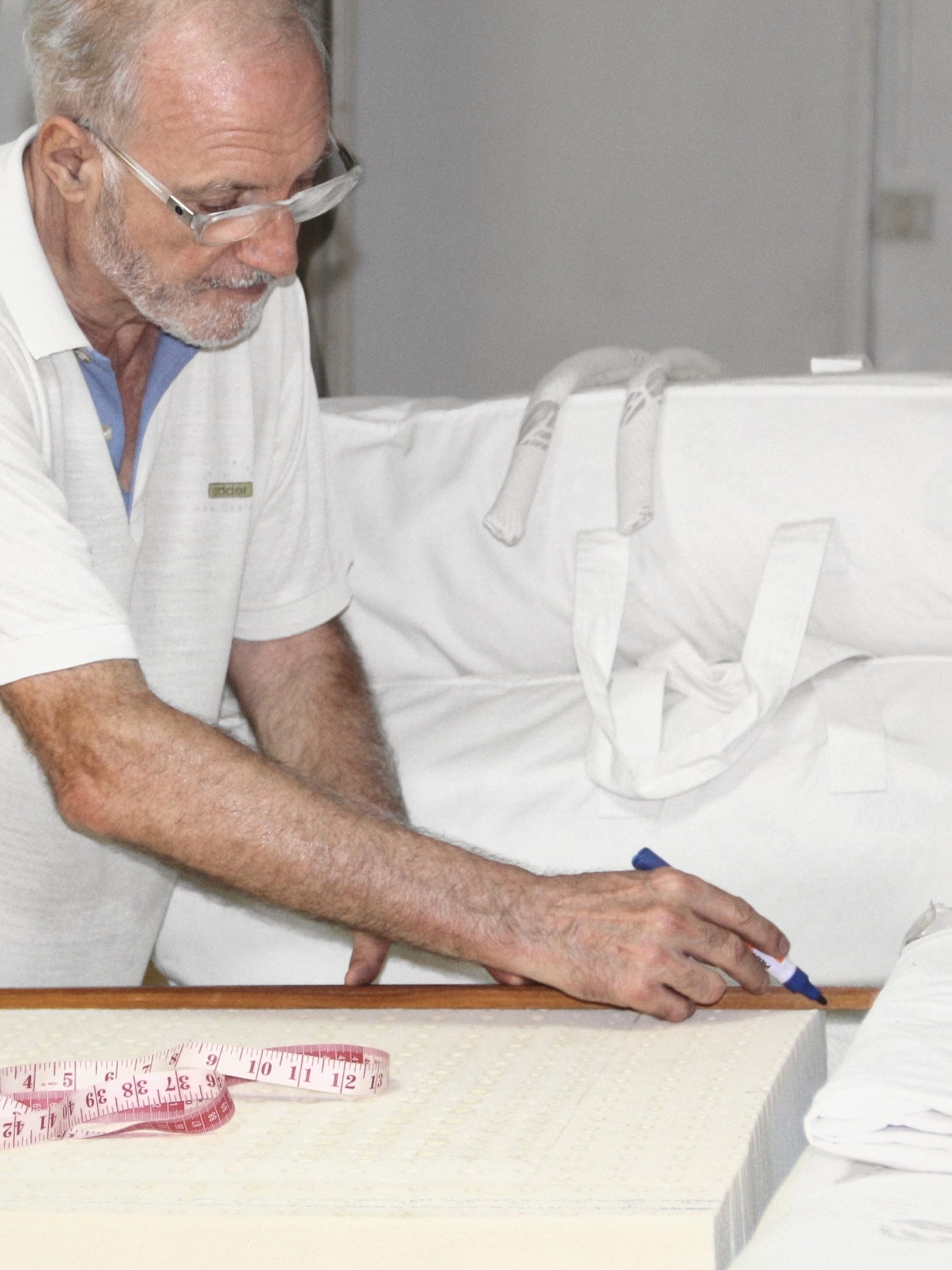 Dominique Bienfait in a white polo and glasses, leaning over a block of latex and drawing a line with a marker along a wooden rule, a tape measure in front of him.