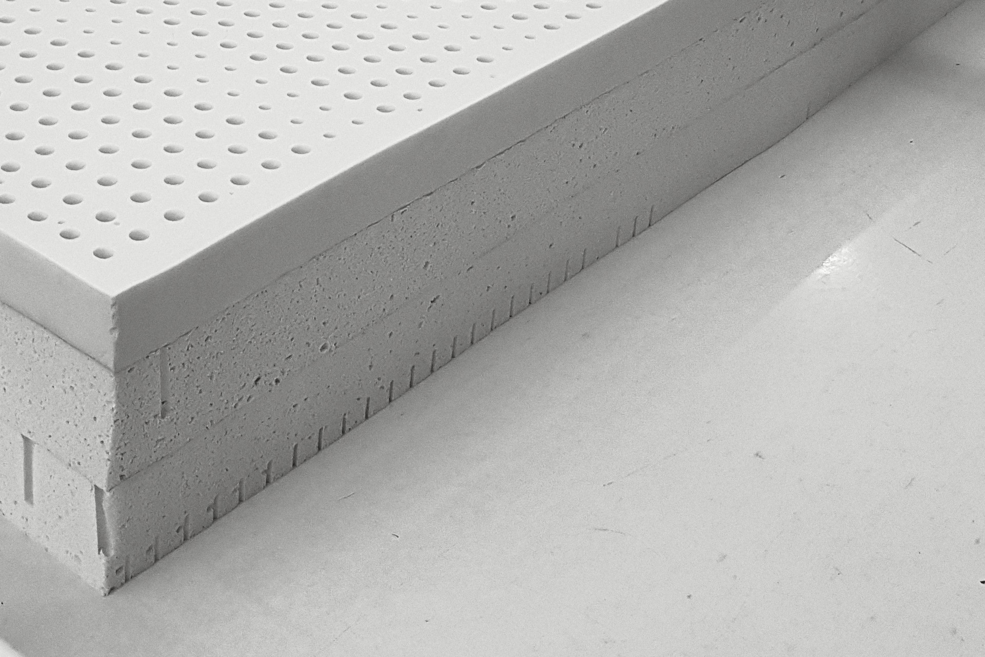 Slabs of natural latex stacked on a white table in a latex factory: rows of pin holes on the top slab, open cells along the cut sides.
