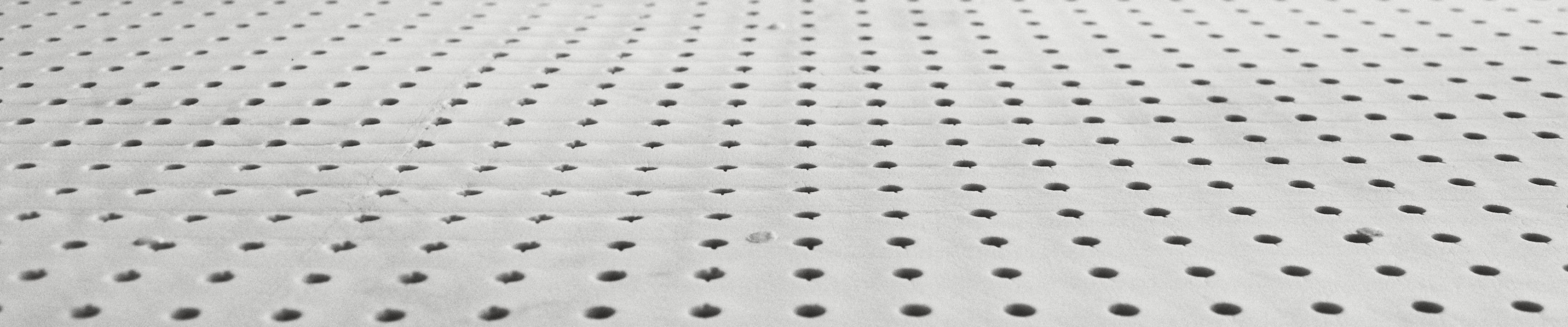 Close view across a sheet of natural latex, rows of round pin holes running away from the camera.
