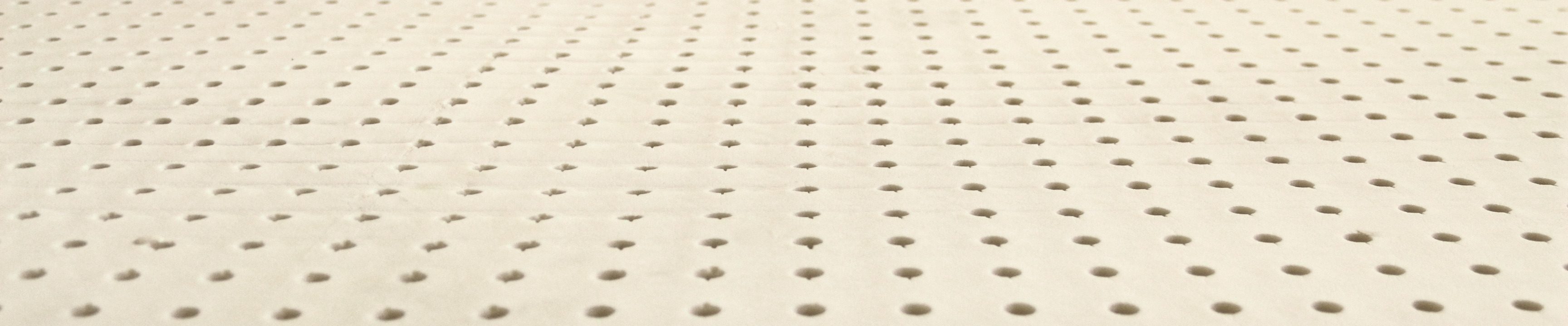 Close view across a sheet of natural latex, rows of round pin holes running away from the camera.