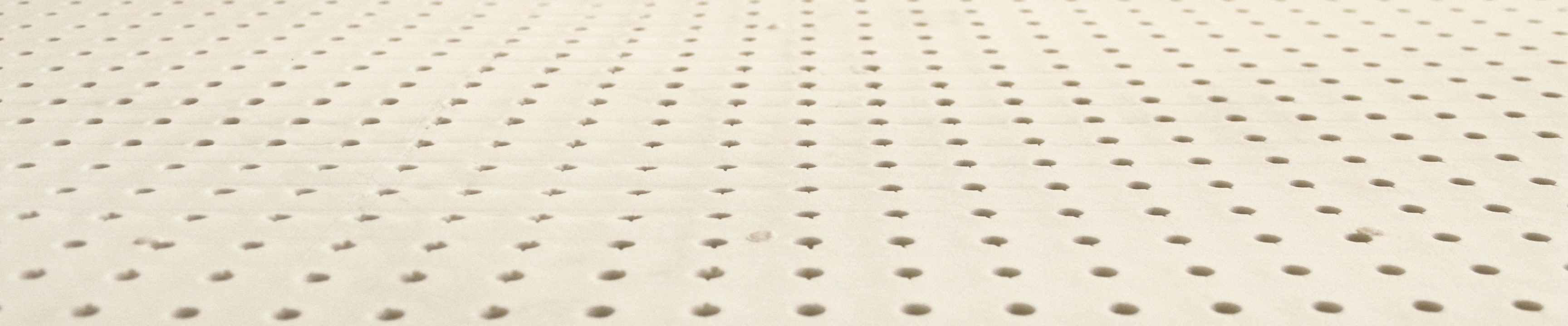 Close view across a sheet of natural latex, rows of round pin holes running away from the camera.