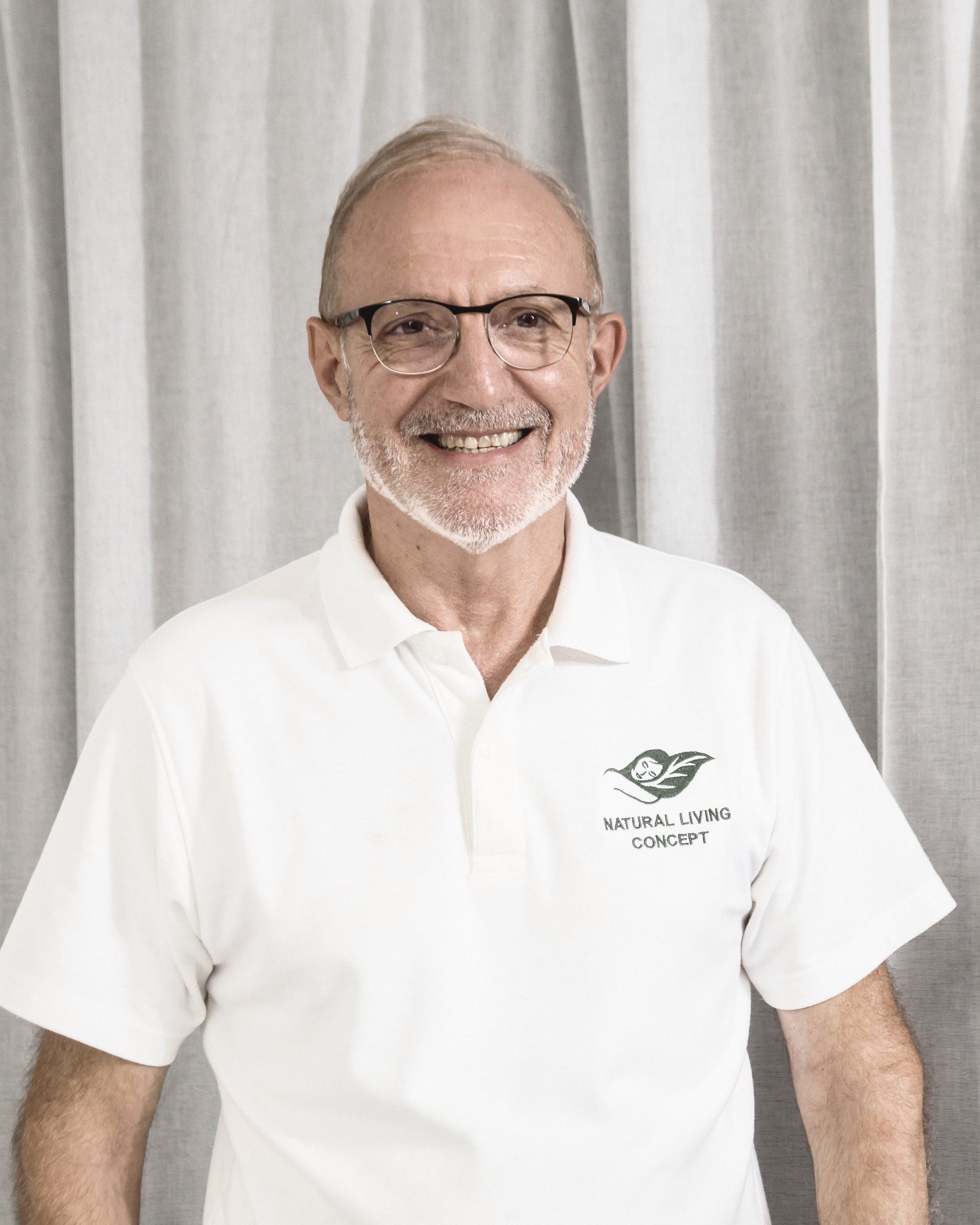 Dominique Bienfait, smiling, in a white Natural Living Concept polo against a white curtain.