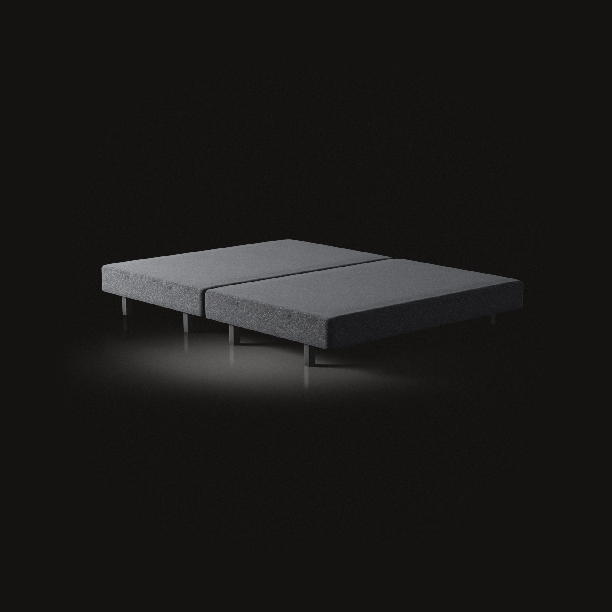 The bed frame on a black floor: an upholstered base in two halves, on short legs.