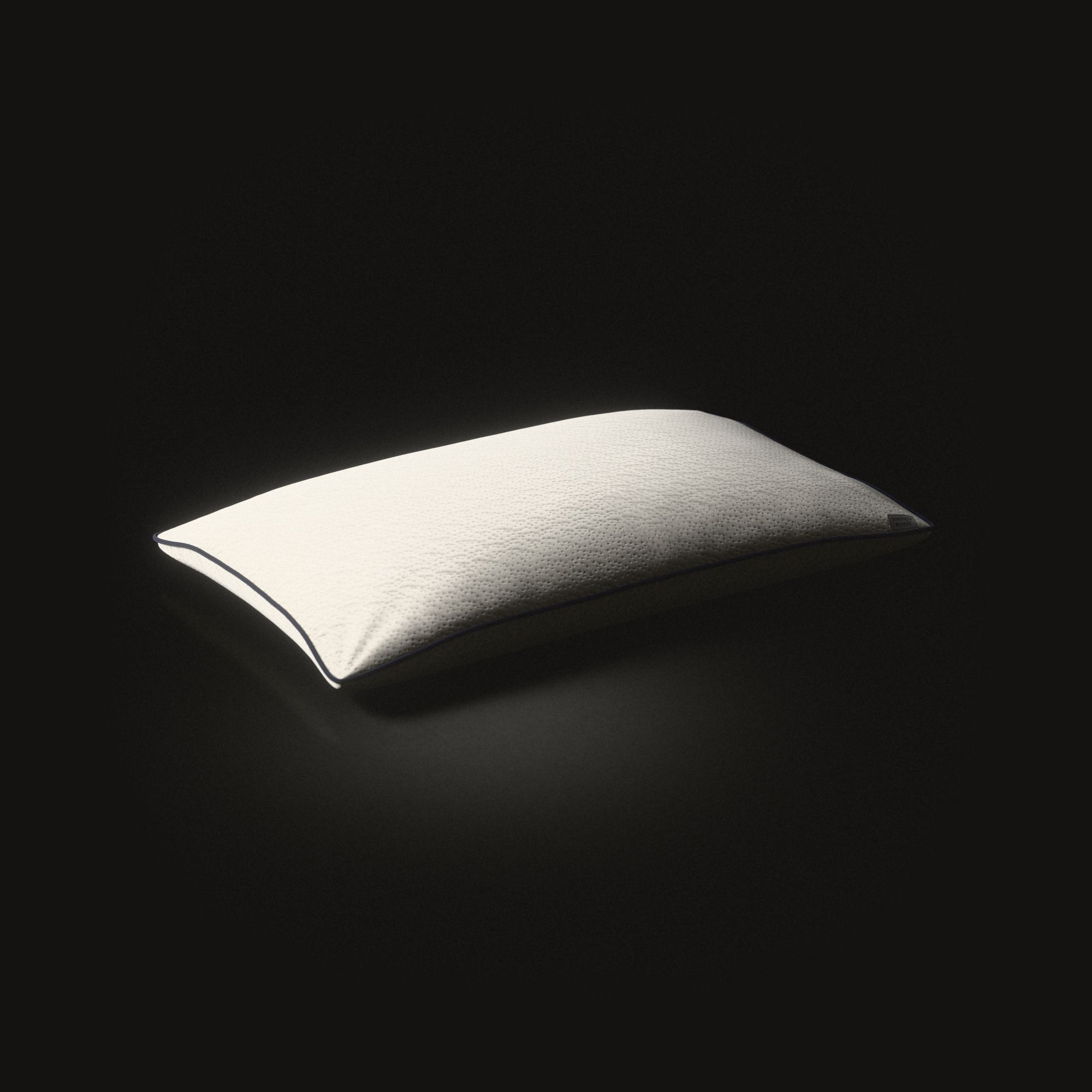 A long cream latex pillow on a black floor, lit from one end: knitted cloth with small pits, a navy cord round its seam.