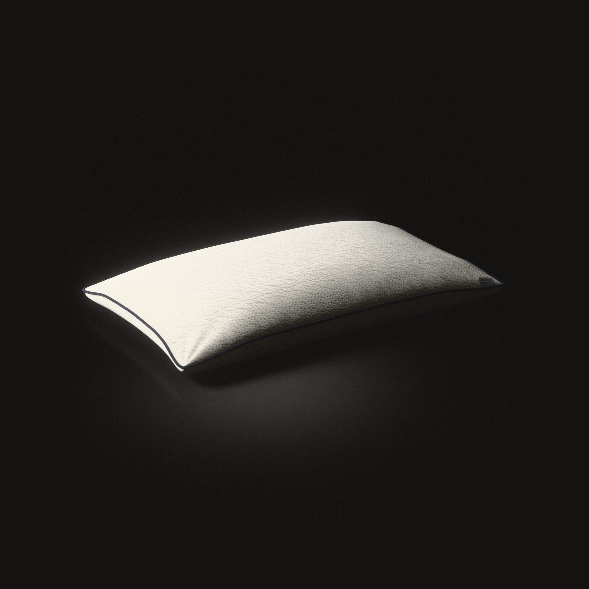 The long King pillow on a black floor, lit from one end: knitted cloth with small pits, a dark cord round its seam.