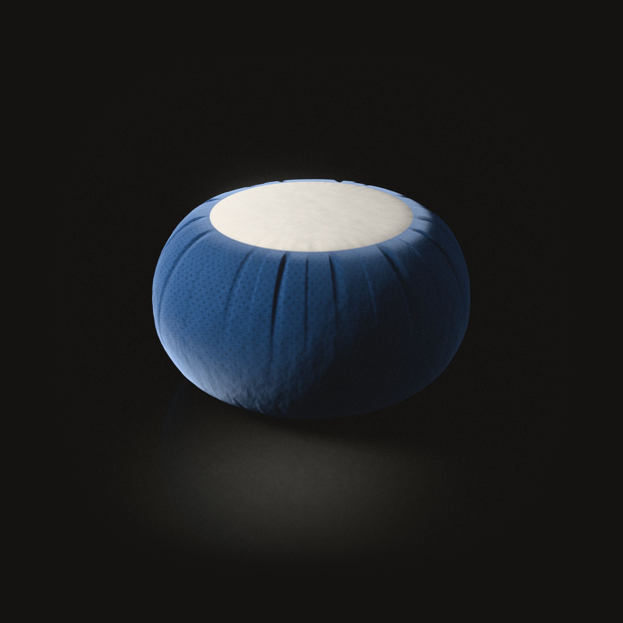 A round blue meditation cushion on a black floor, its side pleated, a flat cream circle of cotton on top.