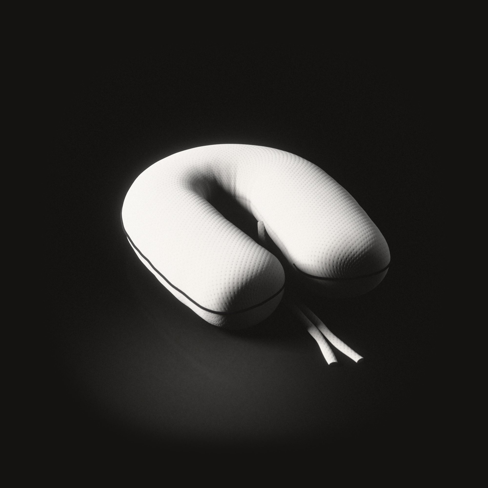 The nursing cushion on a black floor, shaped like a horseshoe, two long ties lying between its ends.