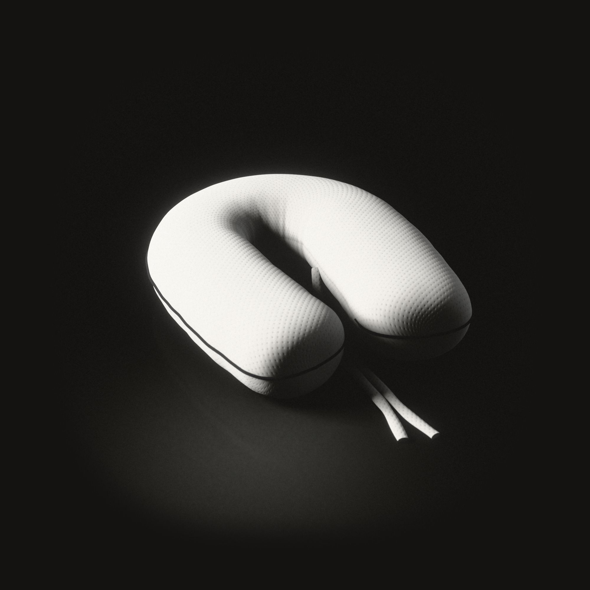 A large white nursing cushion shaped like a horseshoe on a black floor: dotted knitted cloth, a black cord along its outer edge, two long ties lying between its ends.