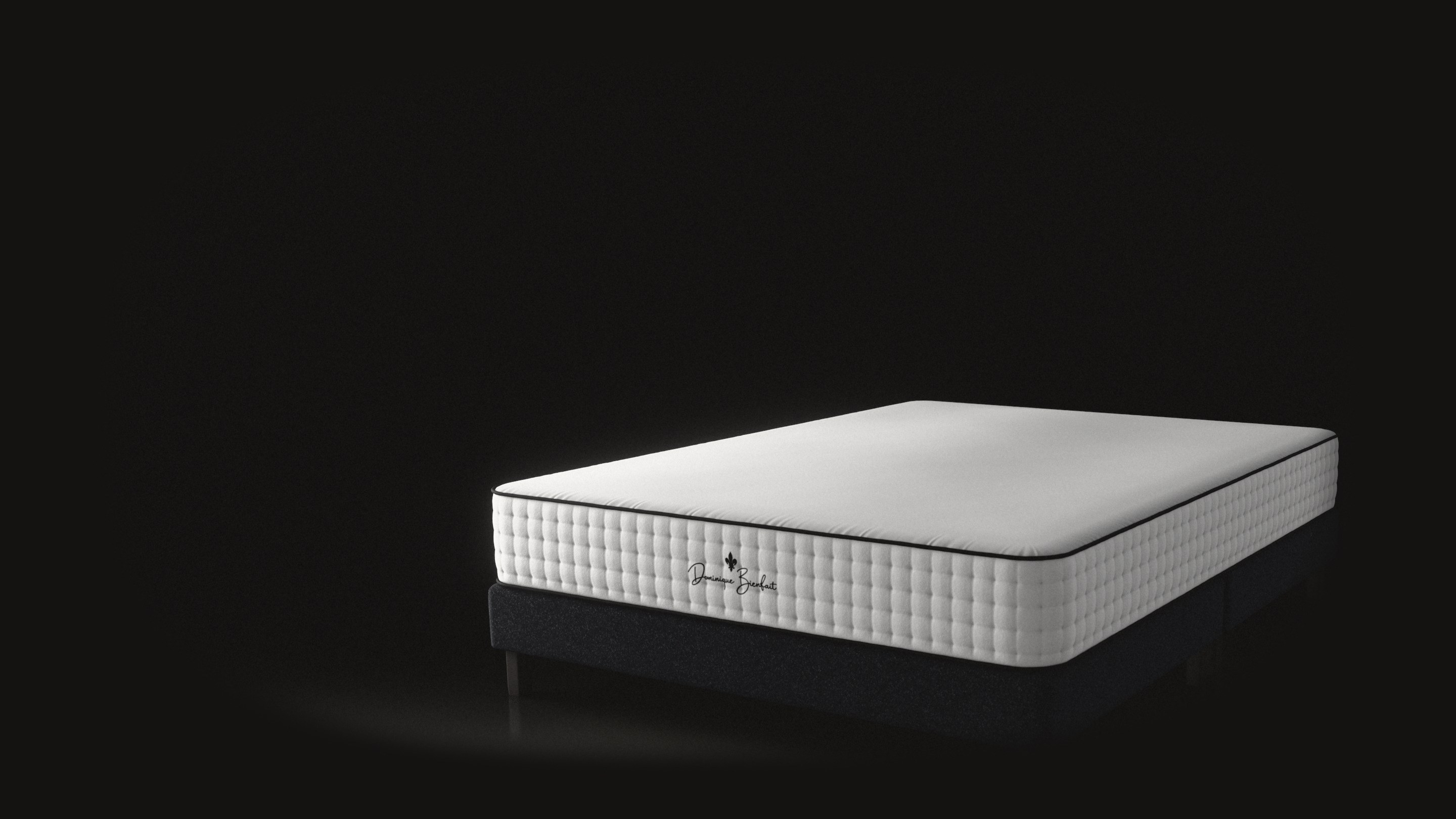 A white mattress with deep tufted sides and black piping on a dark base. On the foot end, a black fleur-de-lis and the handwritten name Dominique Bienfait.