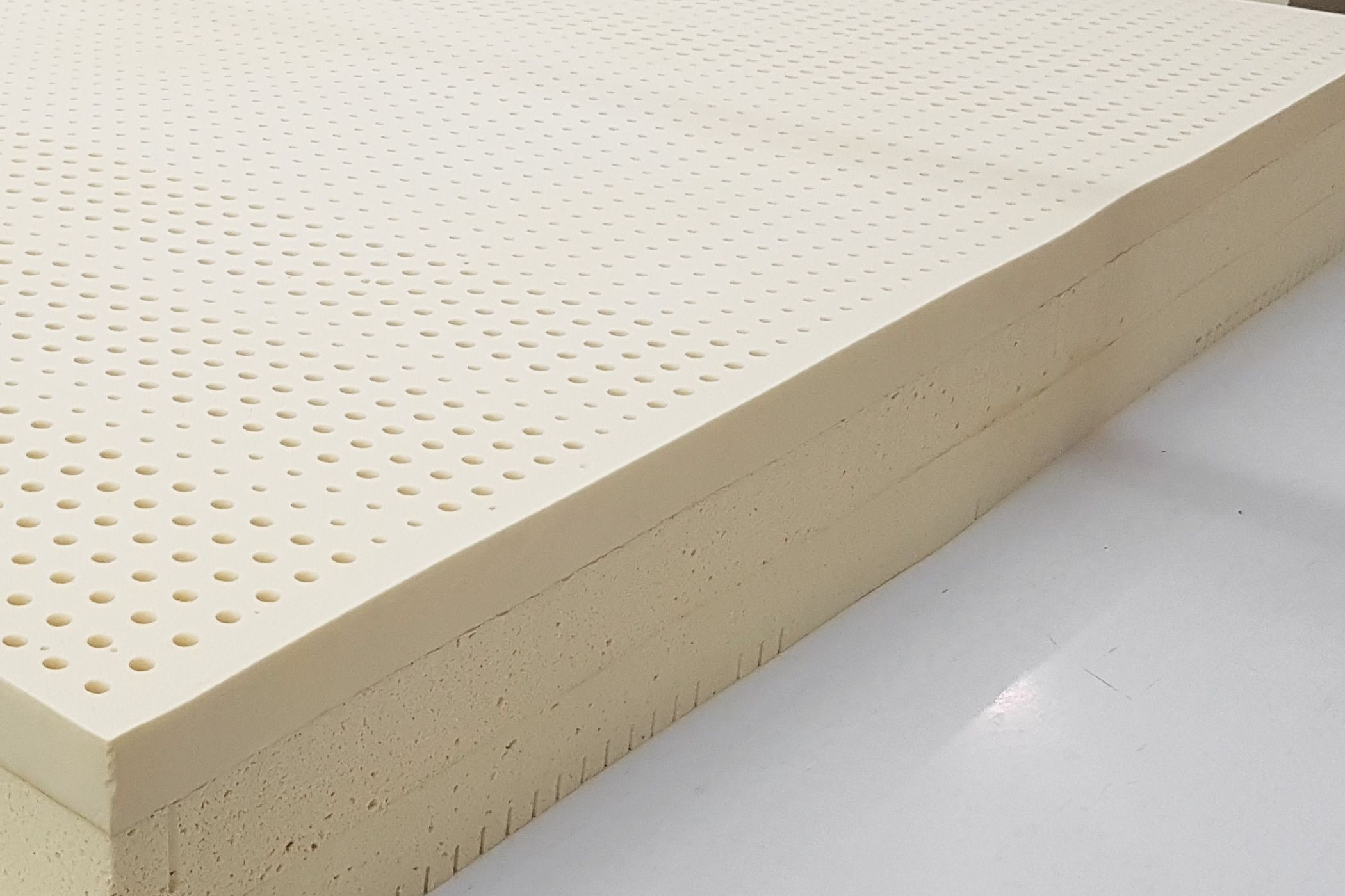 Layers of natural latex stacked on a white table, the top layer covered in rows of pin holes.