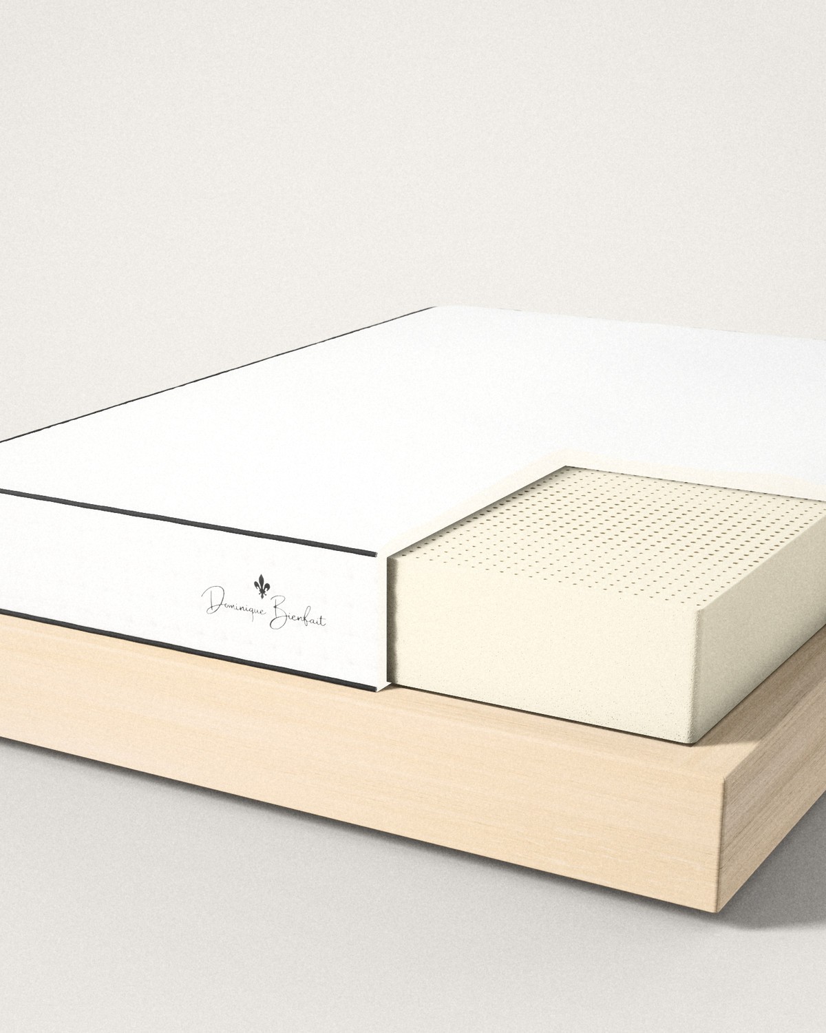A white mattress on a pale oak base, a black fleur-de-lis and the name Dominique Bienfait on its foot end, one corner of the cover cut away to show the cream block of natural latex inside, its top pierced by rows of pin holes.