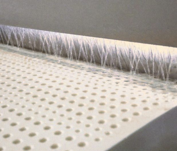 A perforated block of cream latex passing under a curtain of water jets.
