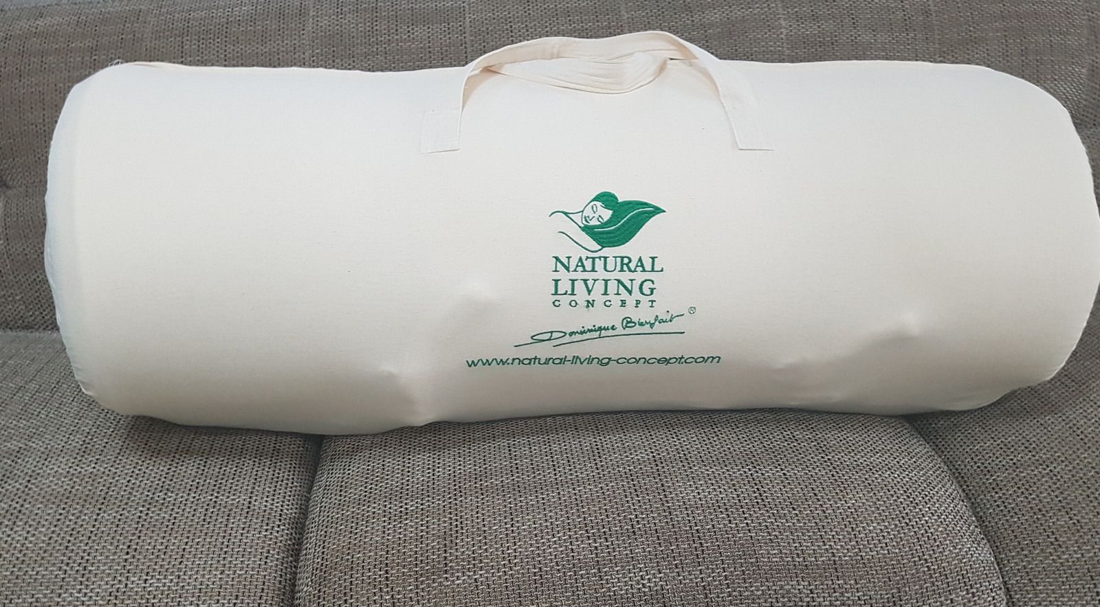 Le traversin dans son sac de transport en coton, imprimé au nom de Natural Living Concept, sur un canapé.