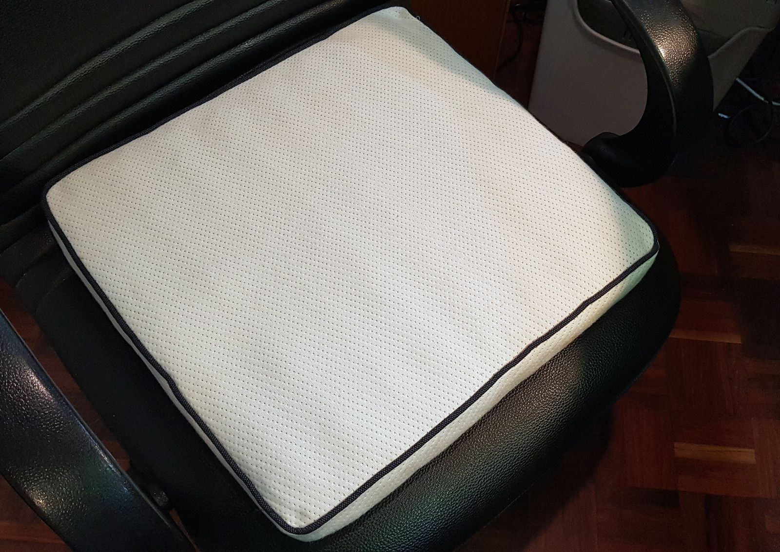 Le coussin d’assise sur une chaise de bureau, sa housse tricotée bordée d’un passepoil sombre.